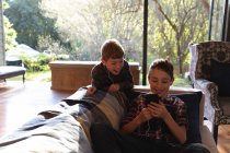 Вид спереду на двох хлопчиків-підлітків за допомогою смартфона та прослуховування музики з навушниками у вітальні вдома — стокове фото
