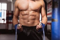 Vista frontal sección media del boxeador masculino sosteniendo una cuerda de salto en un gimnasio de boxeo - foto de stock