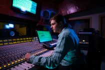Vista lateral de perto de um jovem engenheiro de som caucasiano sentado e trabalhando em uma mesa de mistura em um estúdio de gravação — Fotografia de Stock