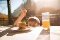 Vista frontal de cerca de un niño caucásico pre adolescente robando una galleta de una mesa durante el desayuno en un jardín - foto de stock