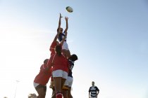 Vue latérale de deux jeunes joueuses de rugby mixtes adultes levées par leurs coéquipières pour attraper le ballon lors d'un match de rugby — Photo de stock