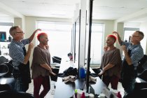 Vue latérale d'un coiffeur masculin caucasien d'âge moyen et d'une jeune femme caucasienne ayant ses cheveux colorés d'un rouge vif dans un salon de coiffure, reflétés dans un miroir — Photo de stock