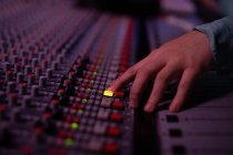 Gros plan de la main d'un ingénieur du son masculin sélectionnant un canal sur un bureau de mixage dans un studio d'enregistrement — Photo de stock