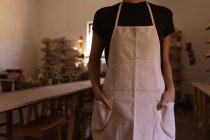 Вид спереду середня секція жіночого гончаря, що стоїть своїми руками в кишенях фартуха в керамічній студії — стокове фото