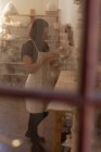 Vue latérale d'une jeune potière caucasienne inspectant un plat dans un atelier de poterie, vue à travers une porte vitrée — Photo de stock