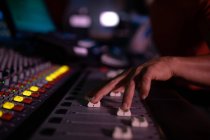 Nahaufnahme der Hand eines männlichen Tontechnikers, der an einem Mischpult in einem Tonstudio drei Faderregler hochschiebt — Stockfoto
