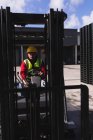 Vista frontal de cerca de un trabajador de la fábrica caucásico de mediana edad utilizando una carretilla elevadora para mover una pila de paletas fuera de un almacén en una fábrica - foto de stock