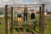 Front view of two young Caucasian women and a young Caucasian man doing pull ups hanging from a frame at an outdoor gym during a bootcamp training session — Stock Photo