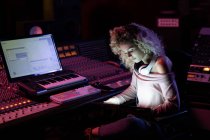 Side view close up of a young Caucasian female sound engineer sitting and working at a mixing desk using a laptop computer in a recording studio — Stock Photo