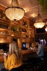 Vue latérale d'un jeune homme et femme caucasien se relaxant en vacances dans un bar, buvant du vin et de la bière à l'aide de smartphones — Photo de stock