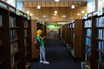 Vista laterale di una giovane studentessa asiatica che indossa un hijab usando uno smartphone in una biblioteca — Foto stock