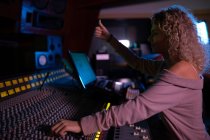 Side view close up of a young Caucasian female sound engineer working at a mixing desk in a recording studio giving a thumbs up sign during a recording session — Stock Photo