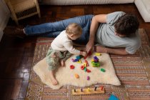 Вид сбоку на молодого кавказского отца, играющего со своим ребенком на полу — стоковое фото