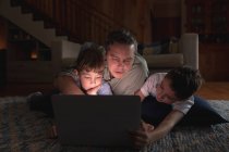 Vista frontal de um homem caucasiano de meia-idade e seus filhos pré-adolescentes usando um computador portátil em uma sala de estar — Fotografia de Stock