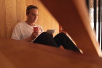 Вид сбоку крупным планом белого мужчины средних лет, сидящего дома на лестнице и пользующегося планшетным компьютером — стоковое фото