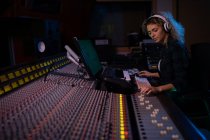 Side view close up of a young Caucasian female sound engineer sitting and working at a mixing desk in a recording studio wearing headphones — Stock Photo