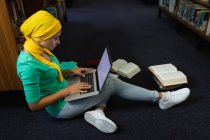Vista lateral de perto de uma jovem estudante asiática vestindo um hijab usando um computador portátil e estudando em uma biblioteca — Fotografia de Stock