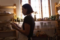 Вид збоку молода кавказька жіноча Поттер з використанням планшета в гончарному студії — стокове фото