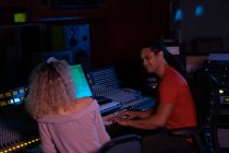 Side view close up of a young mixed race male sound engineer sitting and working with a young Caucasian woman with her back to the camera at a mixing desk in a recording studio — Stock Photo