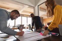Side view close up of a young African American man and a young Caucasian man and woman standing and leaning over a desk working together on a project in a creative office — Stock Photo