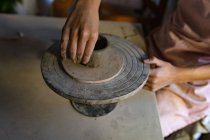 Elevado primer plano de las manos de alfarero hembra formando arcilla en una olla en una rueda de bandas en un estudio de cerámica - foto de stock