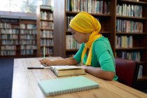 Vista lateral de perto de uma jovem estudante asiática vestindo um hijab fazendo anotações e estudando em uma biblioteca — Fotografia de Stock