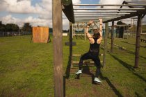 Rear view of a young Caucasian woman hanging from monkey bars at an outdoor gym during a bootcamp training session — Stock Photo