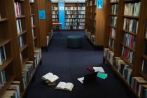 Интерьер библиотеки с рядами книжных полок, сиденьем и книгами и ноутбуком на полу — стоковое фото