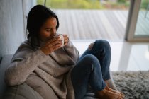 Erhöhte Ansicht einer jungen kaukasischen brünetten Frau, die mit hochgezogenen Beinen auf einem Sofa sitzt und eine Tasse Kaffee genießt — Stockfoto
