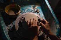 Elevado primer plano de las manos de alfarero femenino utilizando una herramienta para dar forma a la base de un tazón en una rueda de alfarero en un estudio de cerámica - foto de stock