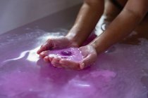 Primo piano delle mani coppettate di una donna in un bagno contenente sali da bagno rosa effervescenti nell'acqua del bagno — Foto stock