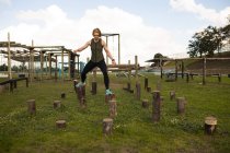 Frontansicht einer jungen kaukasischen Frau, die während eines Bootcamp-Trainings in einem Outdoor-Fitnessstudio zwischen Holzpfosten springt — Stockfoto