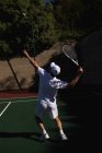 Задній вигляд молодого кавказького чоловіка, який грає в теніс у сонячний день, служить зі стіною за спиною. — стокове фото