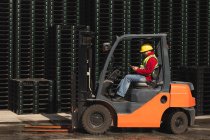 Side view of a middle aged Caucasian male factory worker sitting in a forklift truck using a smartphone beside stacks of pallets outside a warehouse at a factory — Stock Photo