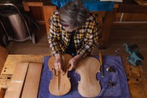 Vista ad alto angolo di una liutaia caucasica anziana che lavora sul corpo di un violino nel suo laboratorio — Foto stock