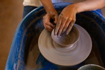 Elevated close up of the hands of female potter shaping wet clay into a bowl shape on a potters wheel in a pottery studio — Stock Photo