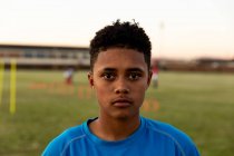 Retrato de cerca de una joven adulta de raza mixta jugadora de rugby de pie en un campo de rugby mirando a la cámara - foto de stock