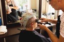 Вид сбоку на белого парикмахера средних лет и молодую белую женщину с подстриженными волосами в парикмахерской, отражённую в зеркале — стоковое фото