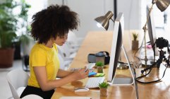Seitenansicht einer jungen Frau mit gemischter Rasse, die an einem Schreibtisch sitzt und in einem kreativen Büro Farbmuster betrachtet — Stockfoto