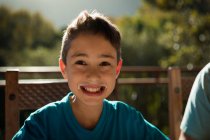 Retrato close-up de um menino pré-adolescente caucasiano sentado em uma mesa em um jardim, sorrindo para a câmera — Fotografia de Stock