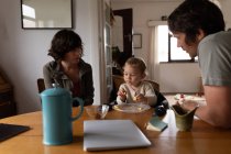 Vue latérale de jeunes parents caucasiens assis à une table et mangeant des bébés — Photo de stock