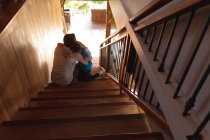 Rear view of a middle aged Caucasian man embracing with his pre teen son sitting on a staircase — Stock Photo