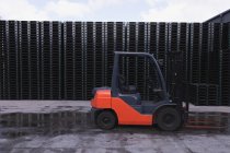 Side view close up of a forklift trucked parked outside in a pallet storage area outside a factory warehouse building — Stock Photo