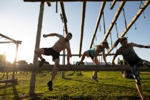 Front view of two young Caucasian women and a young Caucasian man vaulting over a hurdle at an outdoor gym during a bootcamp training session — Stock Photo