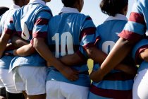 Rear view mid section of a team of female rugby players standing on a rugby field with arms linked preparing for a rugby match — Stock Photo