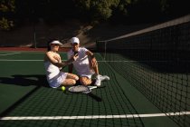 Frontansicht einer jungen kaukasischen Frau und eines Mannes, die an einem sonnigen Tag auf einem Tennisplatz sitzen und ein Selfie machen — Stockfoto