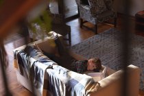 Vista lateral de um menino caucasiano pré-adolescente deitado em um sofá em uma sala de estar e lendo um livro — Fotografia de Stock