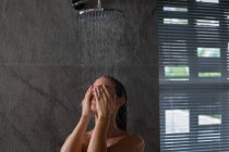 Nahaufnahme einer jungen kaukasischen brünetten Frau, die unter der Dusche steht, die Hände über den Augen in einem modernen Badezimmer — Stockfoto