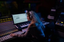 Side view close up of a young Caucasian female sound engineer sitting and working at a mixing desk in a recording studio wearing headphones — Stock Photo