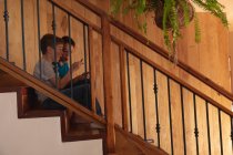 Seitenansicht von zwei vorjugendlichen kaukasischen Jungen, die zu Hause auf einer Treppe sitzen und ein Smartphone benutzen — Stockfoto